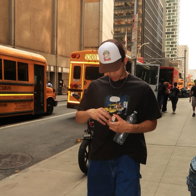 Joseph wearing a cap on a city sidewalk beside yellow school buses